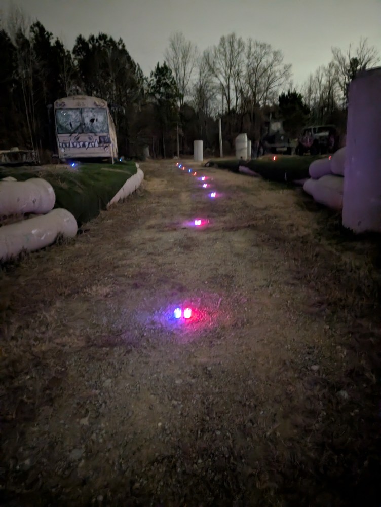 Pathway with colorful ground lights at night in a wooded area, old bus at the end.